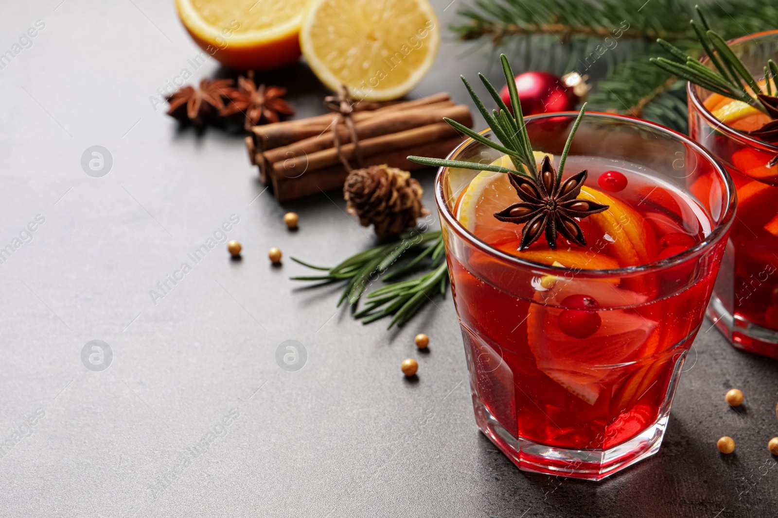 Photo of Delicious punch drink with cranberries, orange and spices on grey table. Space for text