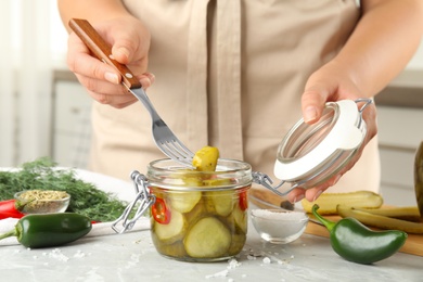 Photo of Woman taking pickled cucumber from jar at table in kitchen, closeup view
