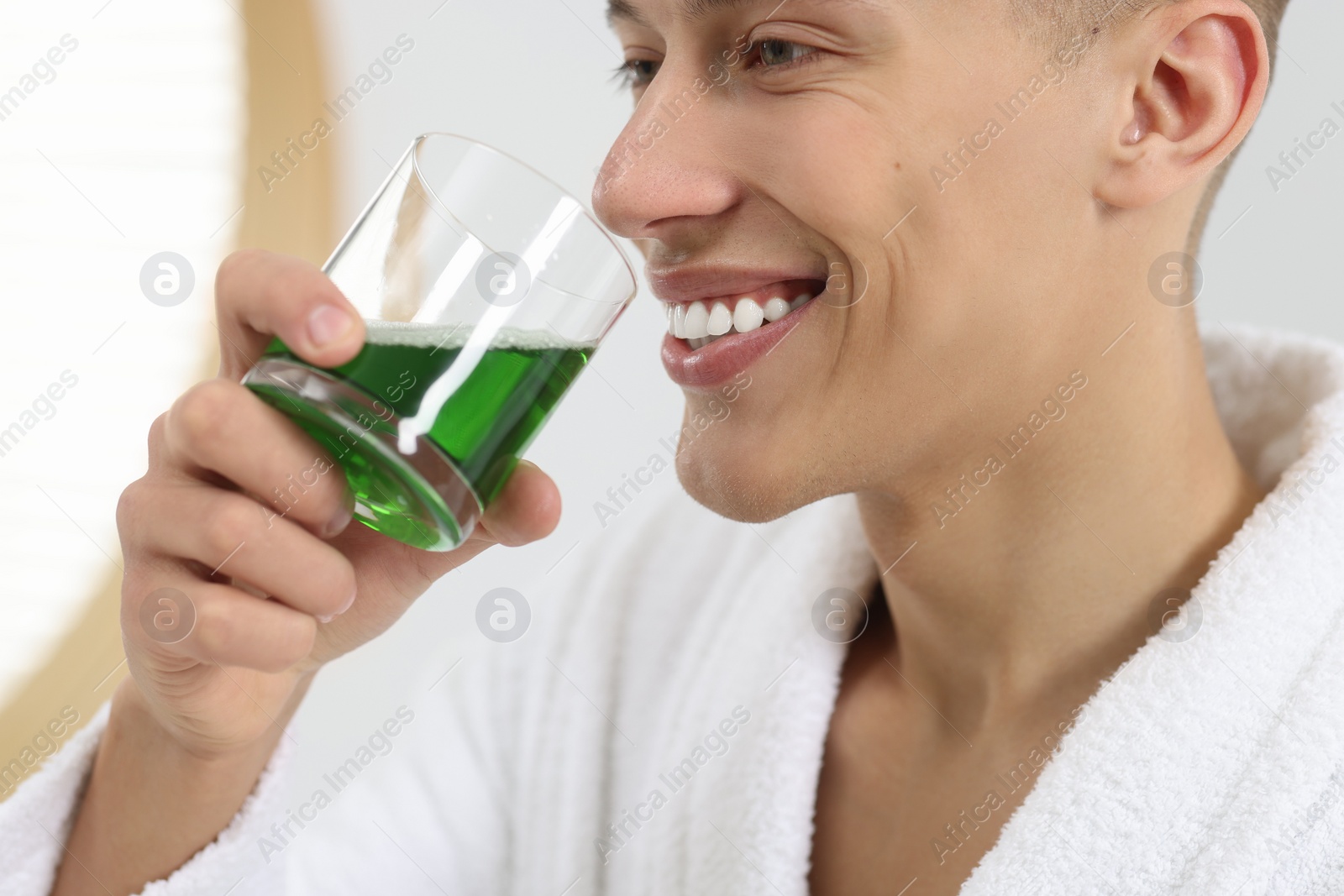 Photo of Young man using mouthwash indoors, closeup view