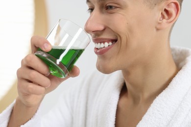 Photo of Young man using mouthwash indoors, closeup view