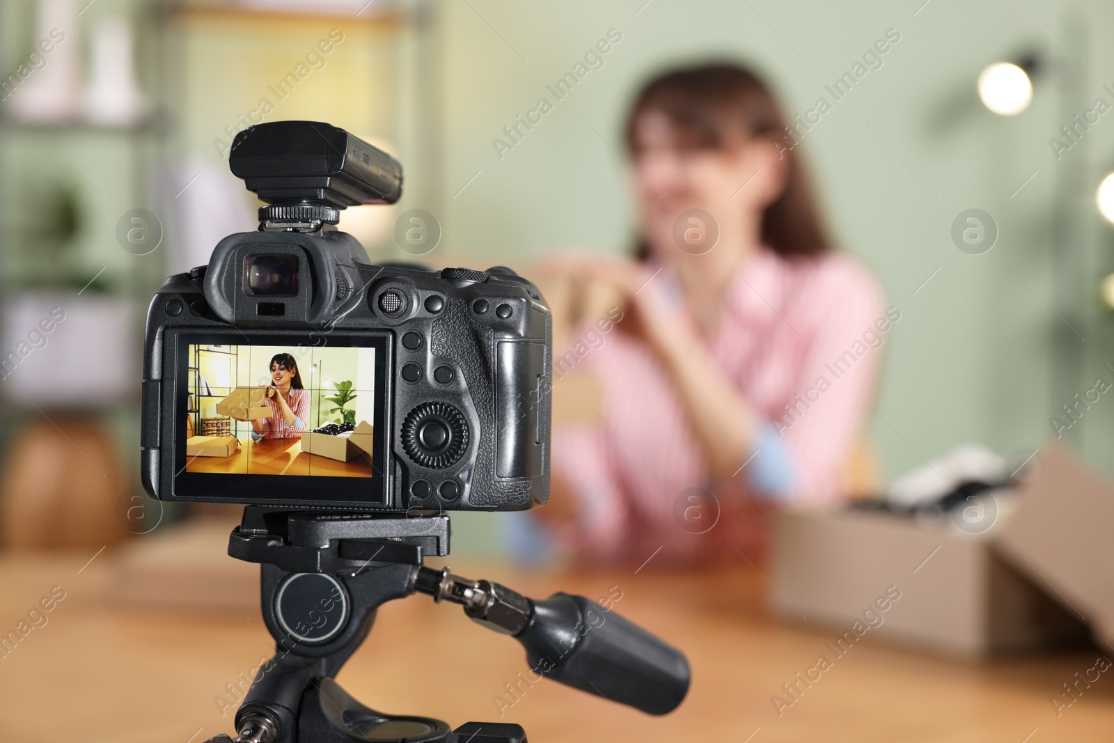 Photo of Fashion blogger recording video while unboxing parcel at home, focus on camera