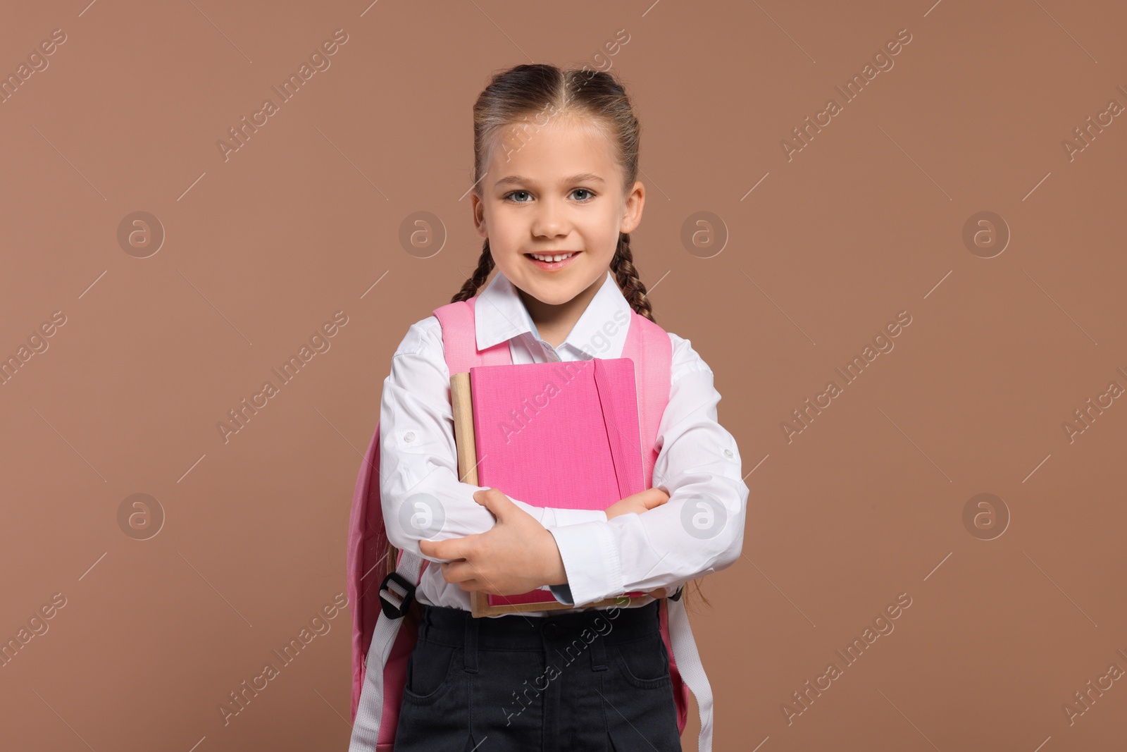 Photo of Happy schoolgirl with backpack and books on brown background