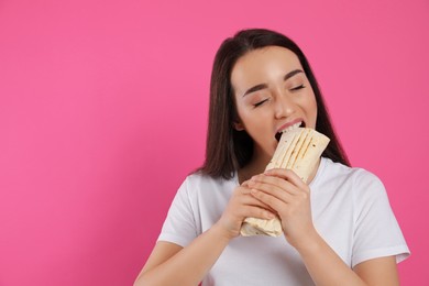 Photo of Young woman eating tasty shawarma on pink background. Space for text