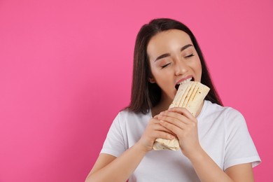 Young woman eating tasty shawarma on pink background. Space for text