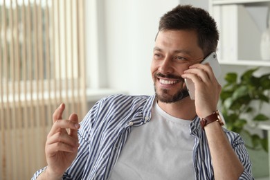 Photo of Happy handsome man talking on smartphone indoors