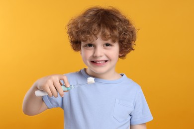 Photo of Cute little boy holding electric toothbrush with paste on yellow background