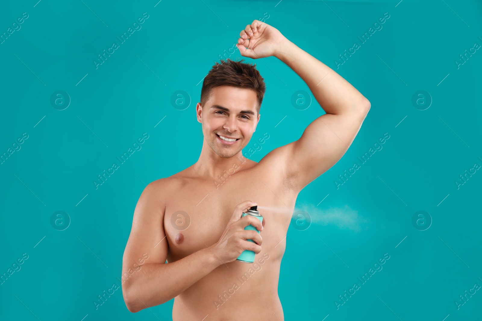 Photo of Young man applying spray deodorant to armpit on blue background