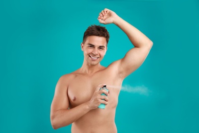 Young man applying spray deodorant to armpit on blue background