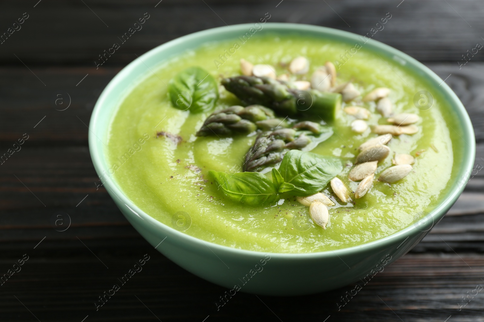 Photo of Delicious asparagus soup in bowl on black wooden table