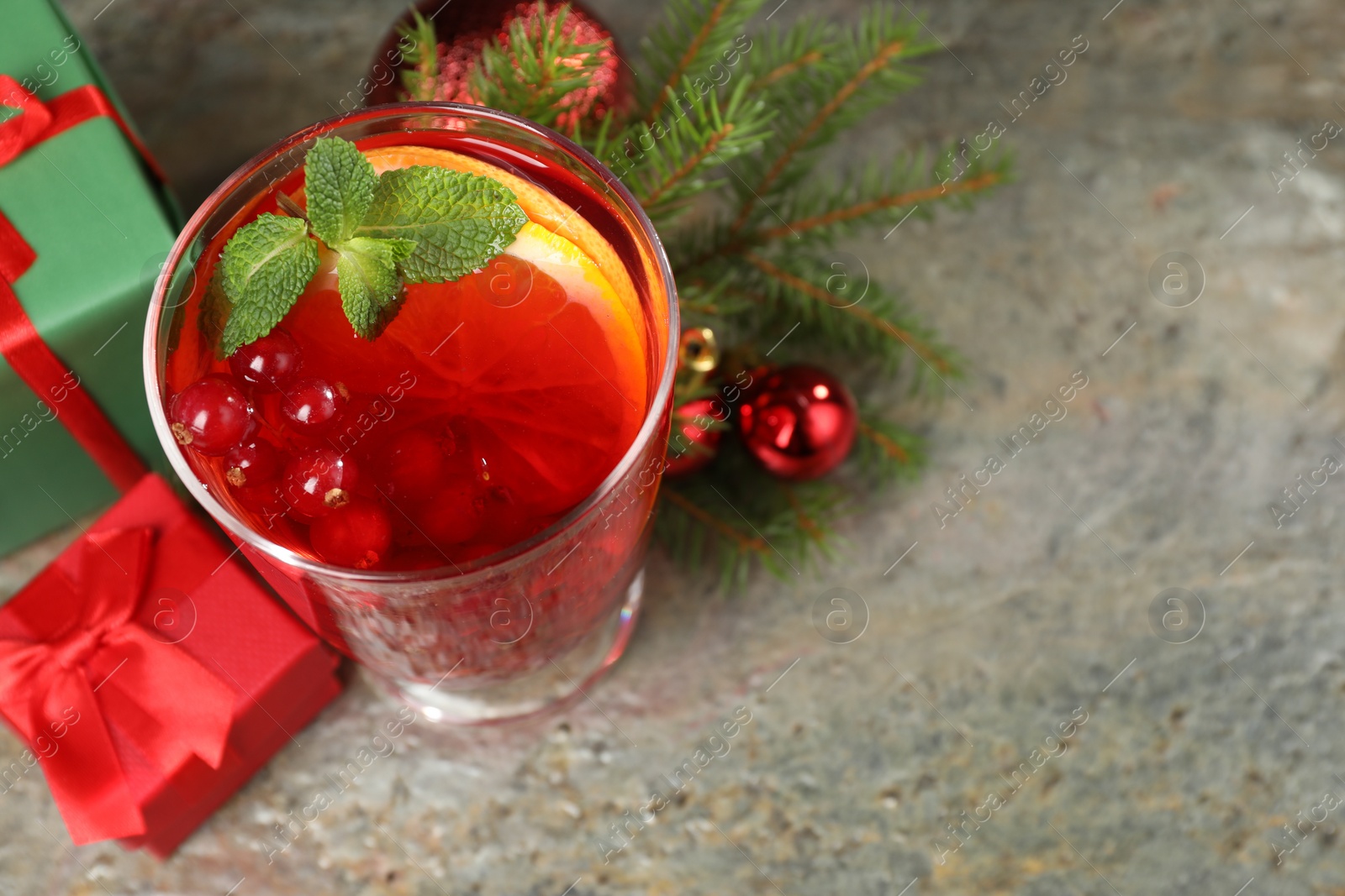 Photo of Aromatic Christmas Sangria in glass, gift boxes and festive decor on grey textured table, above view. Space for text