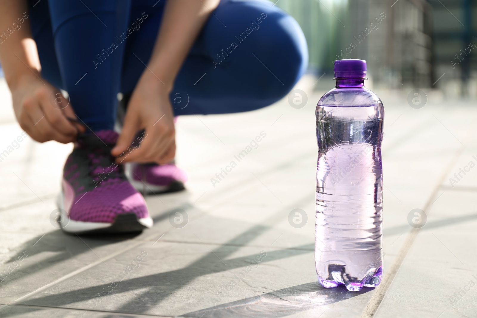 Photo of Plastic bottle of pure water and athletic woman outdoors, closeup