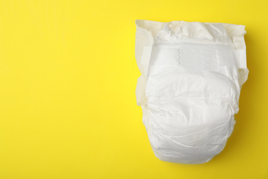 Photo of Baby diaper on yellow background, top view. Space for text