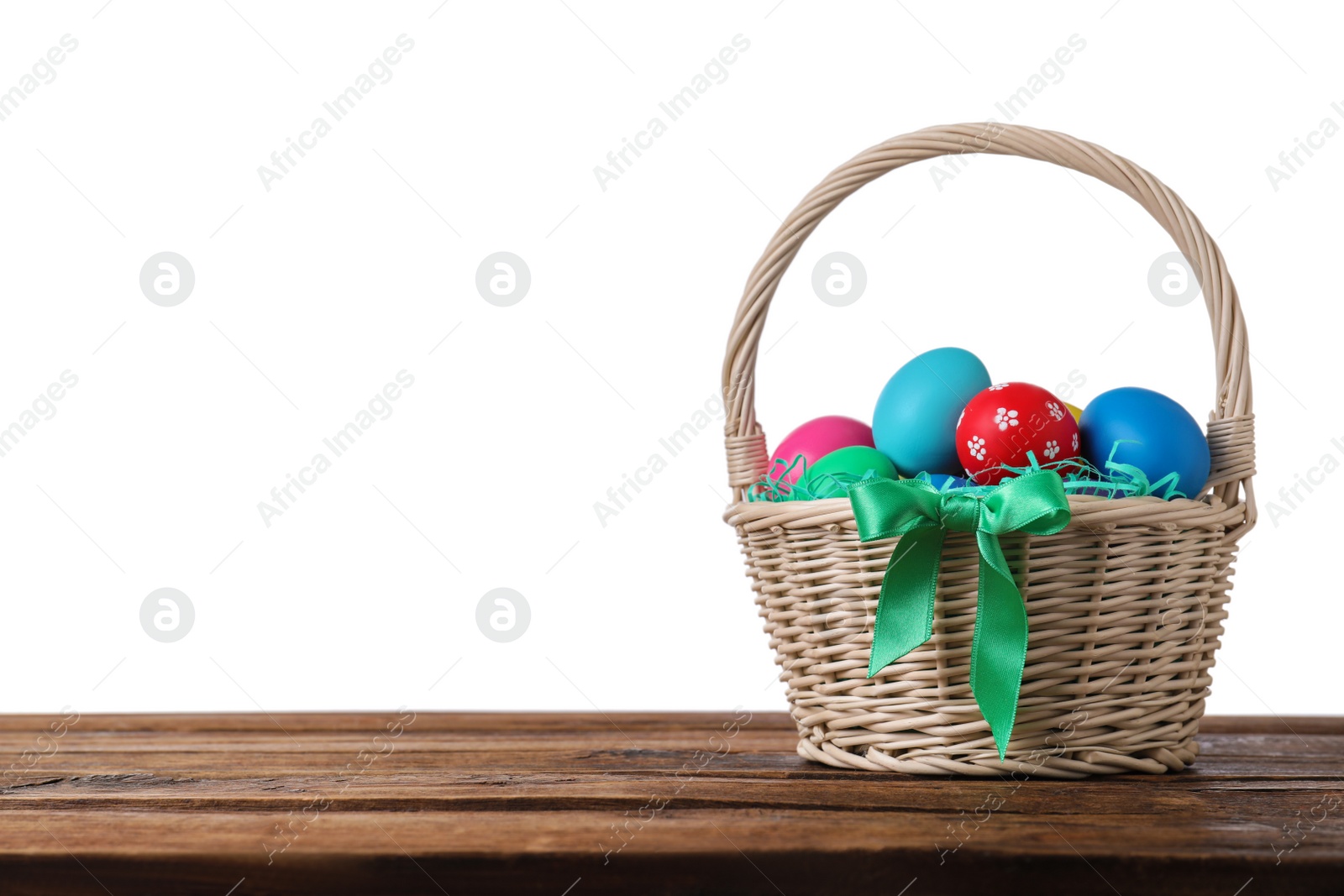 Photo of Colorful Easter eggs in wicker basket on wooden table against white background