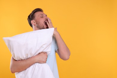 Photo of Sleepy man with pillow yawning on yellow background, space for text. Insomnia problem