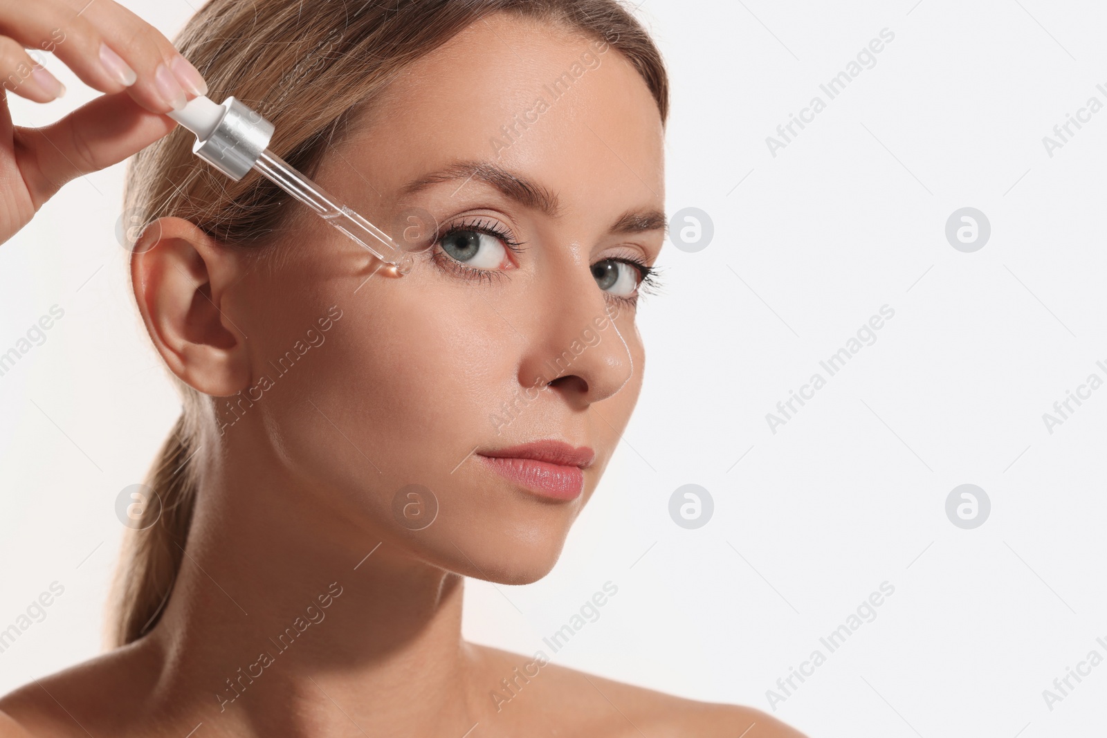 Photo of Beautiful woman applying cosmetic serum onto her face on white background, closeup. Space for text