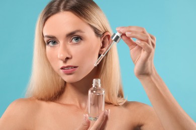 Photo of Beautiful woman with cosmetic serum in her hands on light blue background