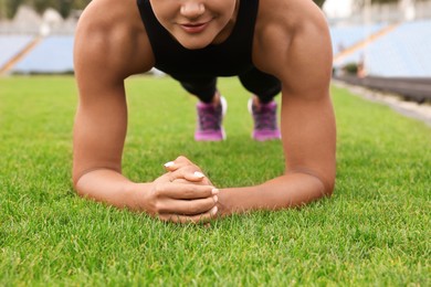 Young woman doing plank exercise on grass at stadium, closeup