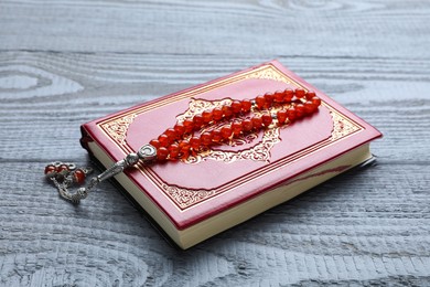 Muslim prayer beads and Quran on grey wooden table