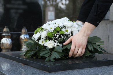 Woman putting funeral wreath of flowers on granite tombstone in cemetery, closeup