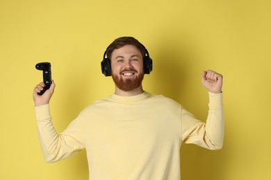 Photo of Happy man in headphones with game controller on pale yellow background