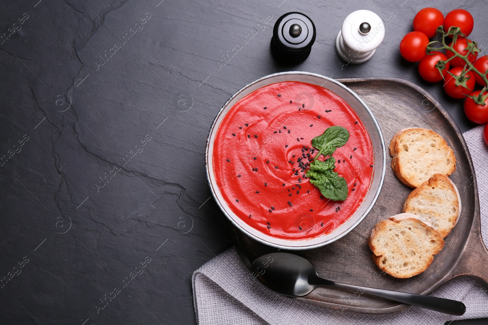 Photo of Delicious tomato cream soup with bread on black table, flat lay. Space for text