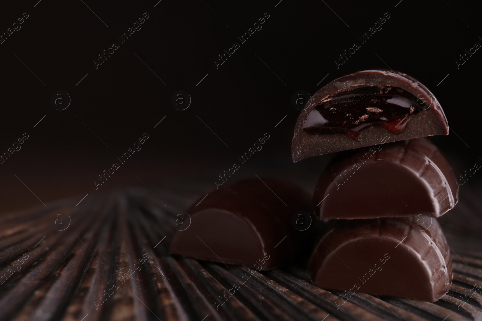 Photo of Tasty dark chocolate candies with jelly filling on wooden board, closeup. Space for text