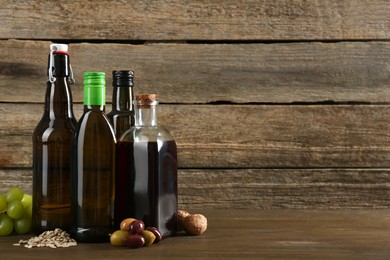 Photo of Vegetable fats. Different cooking oils in glass bottles and ingredients on wooden table, space for text