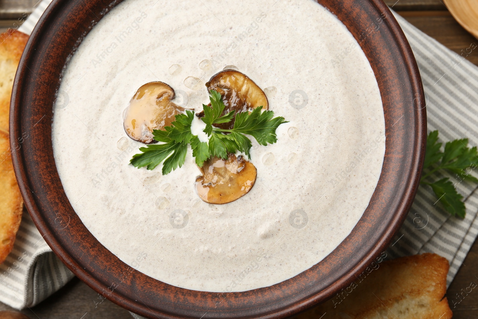 Photo of Fresh homemade mushroom soup in ceramic bowl on wooden table, top view