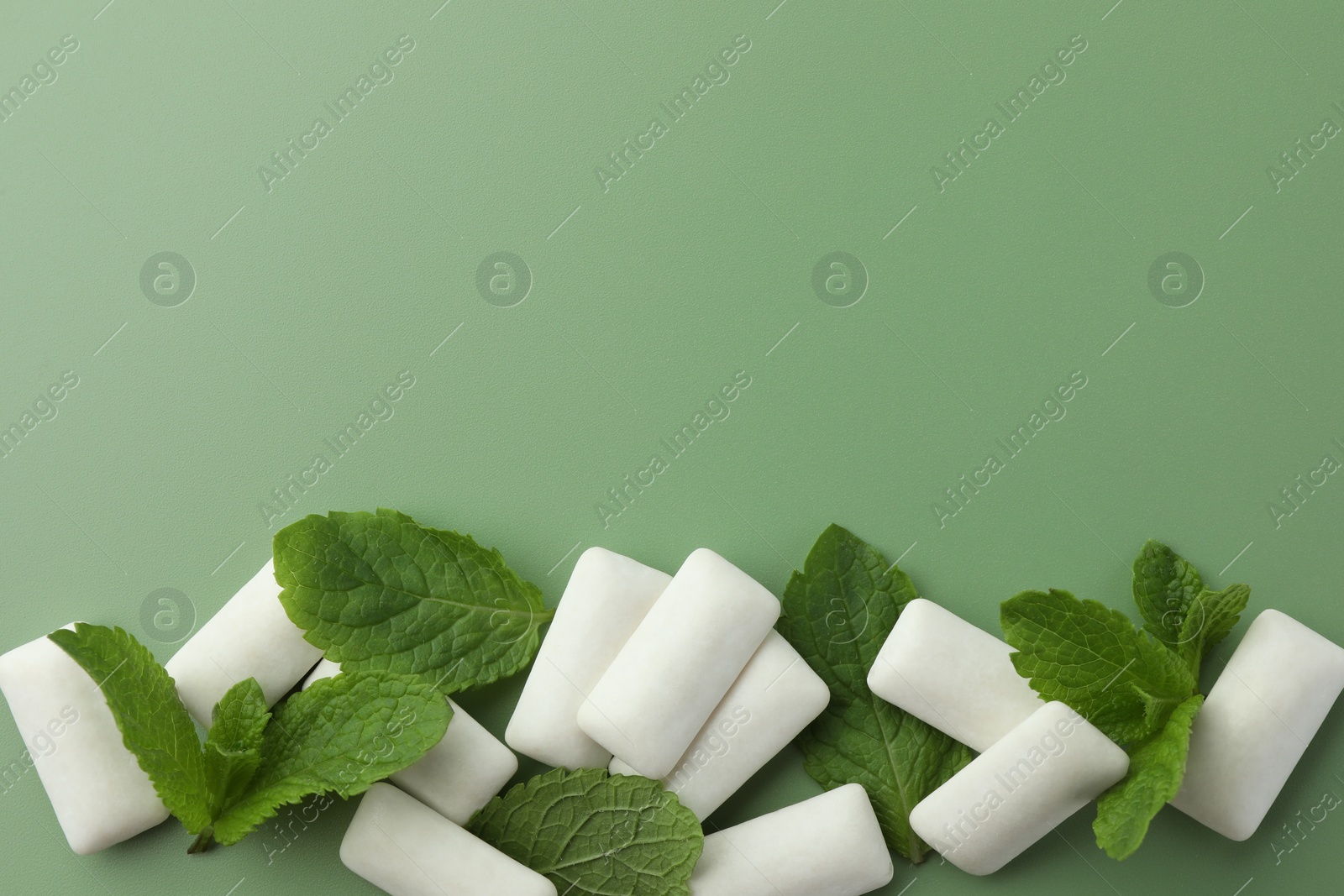 Photo of Tasty white chewing gums and mint leaves on light green background, flat lay. Space for text