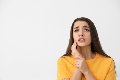 Young woman suffering from strong tooth pain on light background, space for text