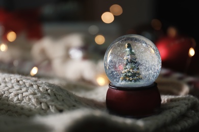 Photo of Christmas snow globe with knitting clothes on blurred background. Space for text