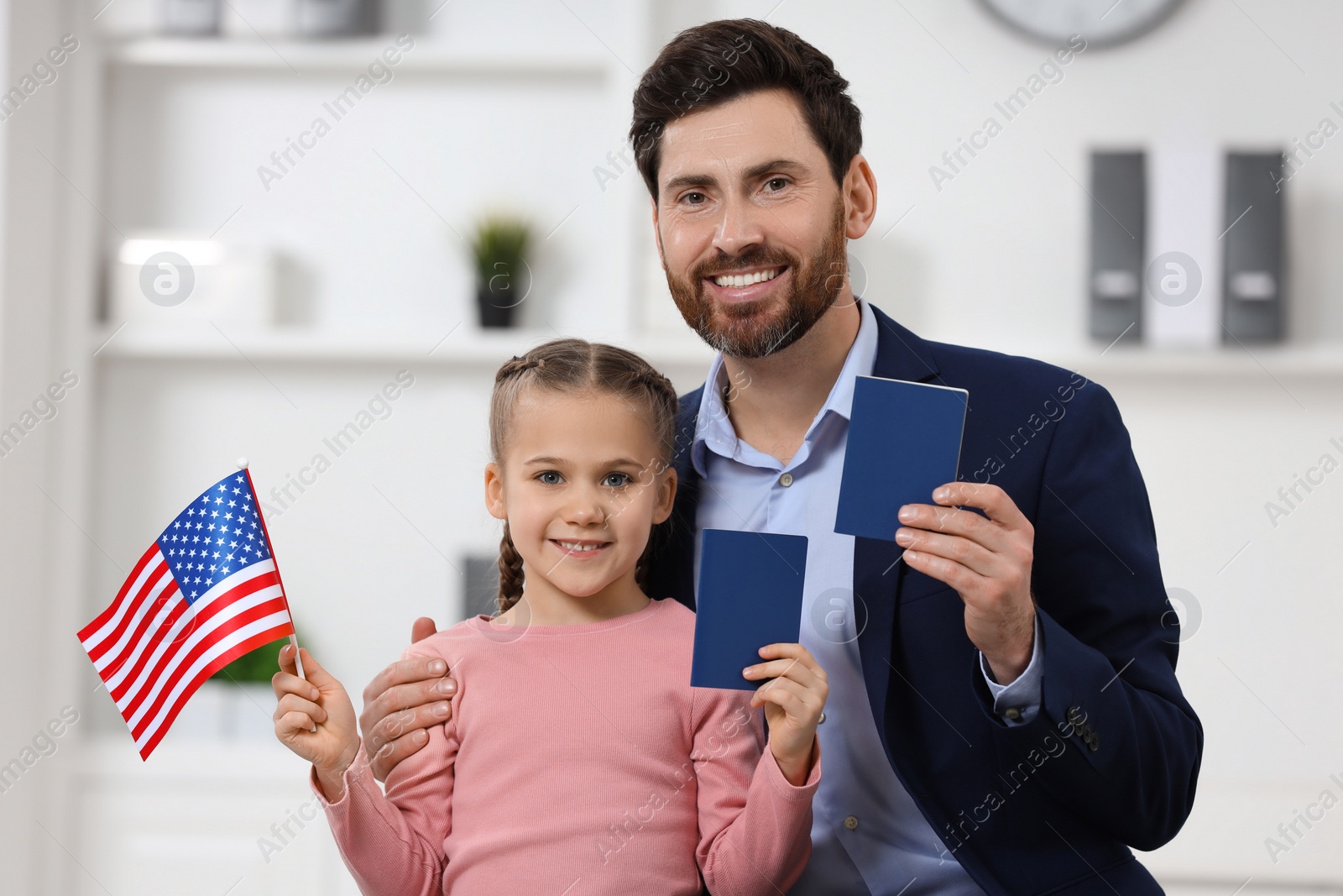 Photo of Immigration. Happy man with his daughter holding passports and American flag indoors