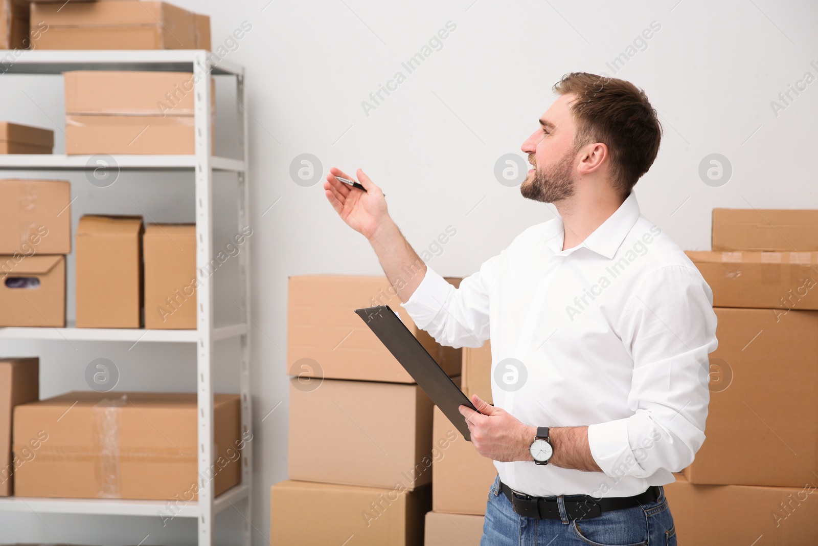 Photo of Young businessman with clipboard near cardboard boxes at warehouse