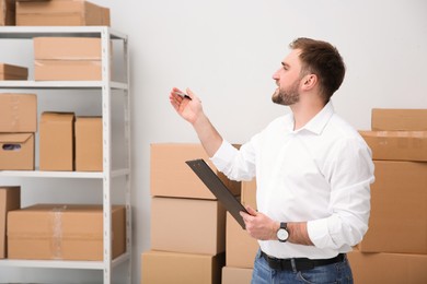 Photo of Young businessman with clipboard near cardboard boxes at warehouse