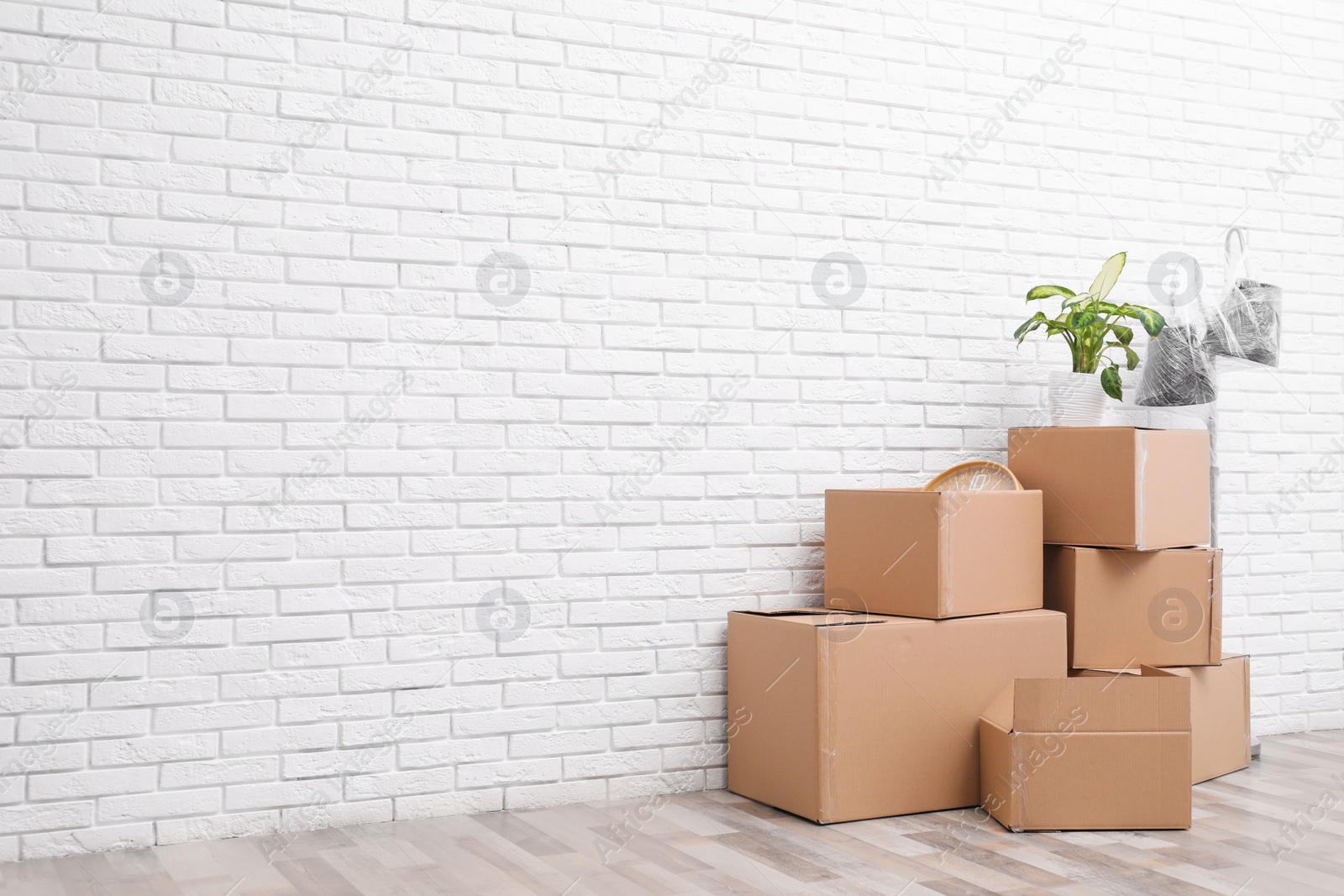 Photo of Pile of cardboard boxes and houseplant near white brick wall, space for text. Moving day