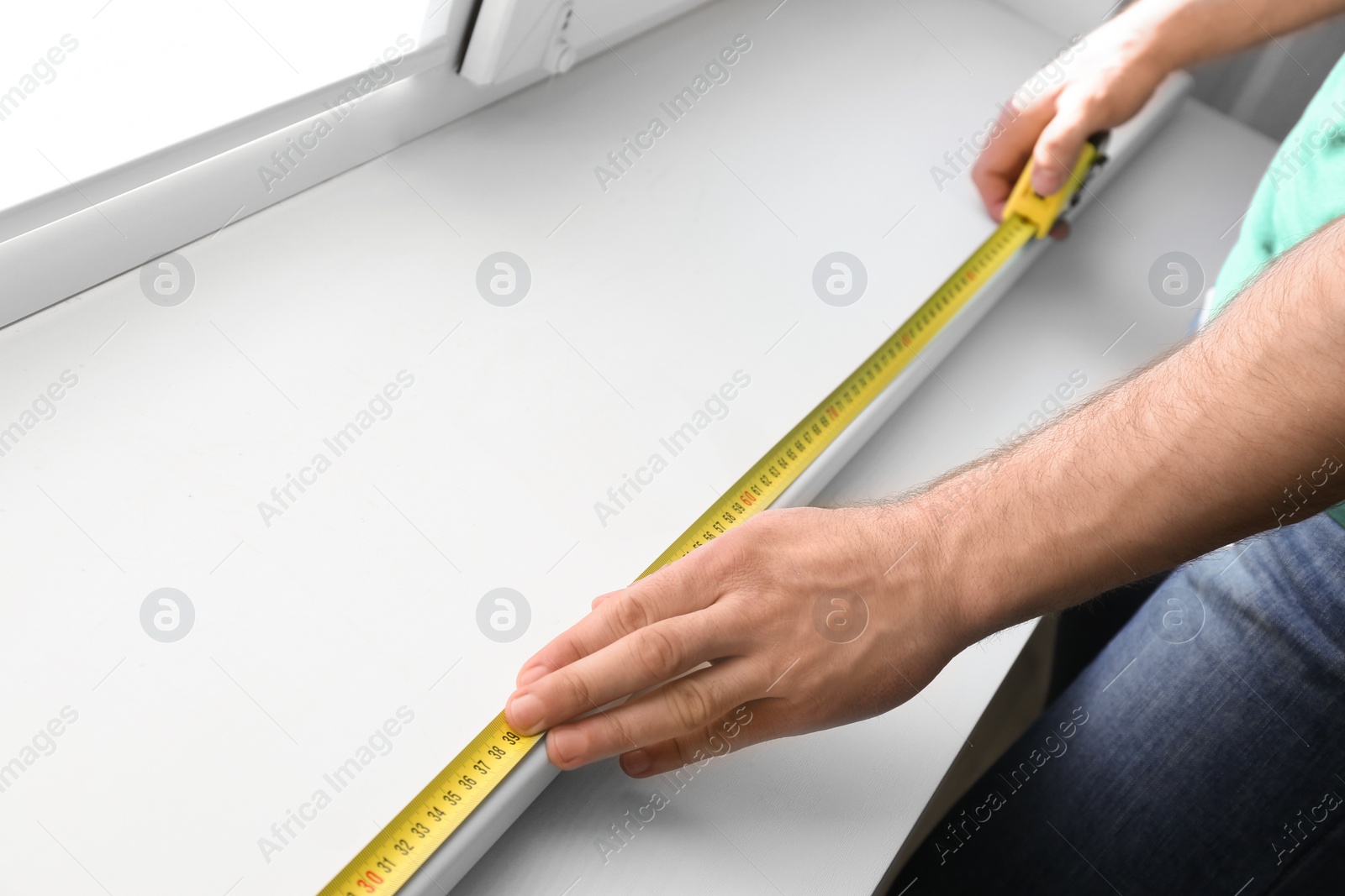Photo of Man measuring white windowsill indoors, closeup. Construction tool