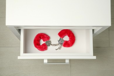 Photo of Red furry handcuffs and keys in drawer indoors, top view. Sex toy