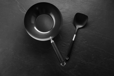 Photo of Black metal wok and spatula on dark textured table, top view