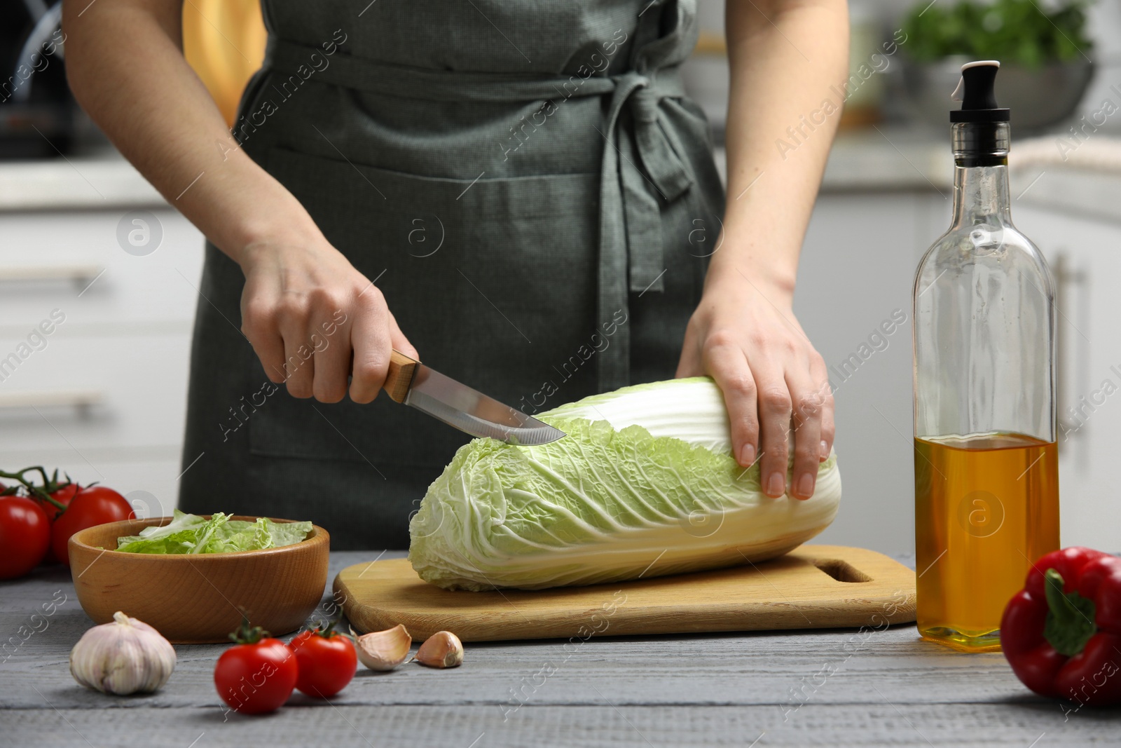 Photo of Woman cutting fresh chinese cabbage at grey wooden table in kitchen, closeup