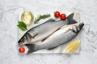 Photo of Sea bass fish and ingredients on white marble table, top view