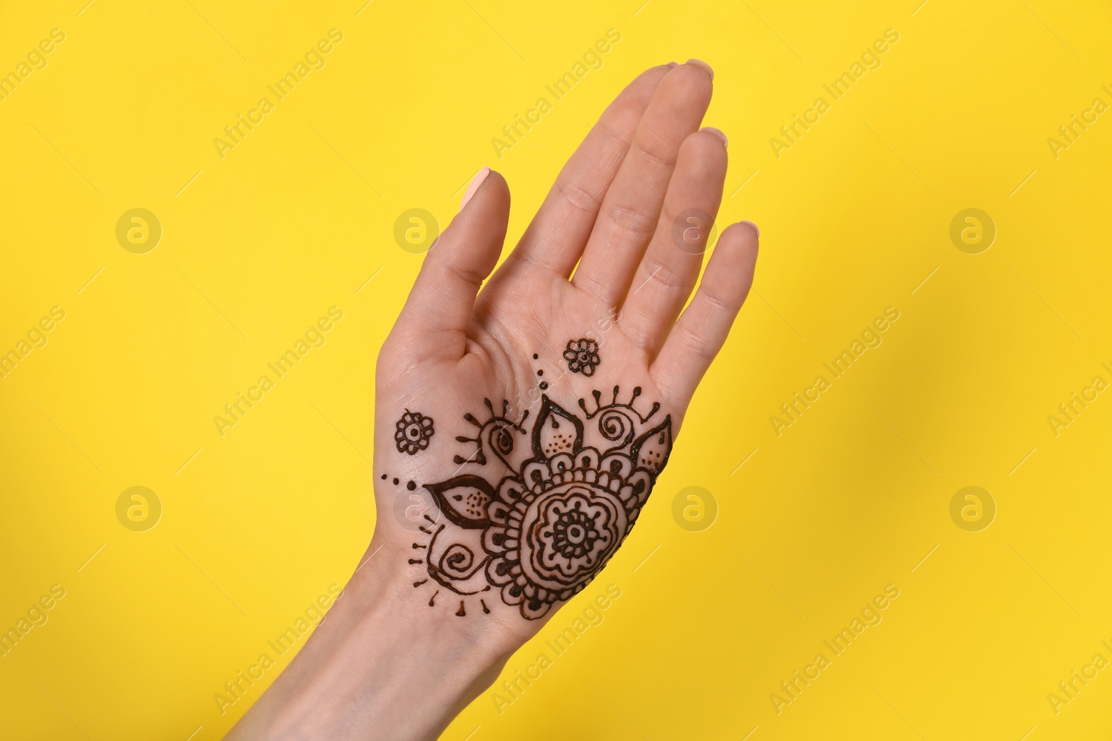 Photo of Woman with henna tattoo on palm against yellow background, closeup. Traditional mehndi ornament