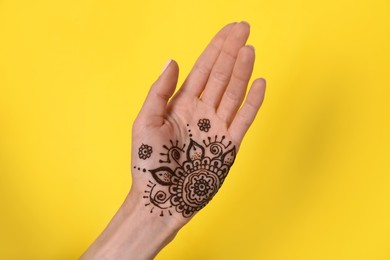 Woman with henna tattoo on palm against yellow background, closeup. Traditional mehndi ornament