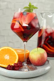 Photo of Glass of Red Sangria and fruits on table near white brick wall