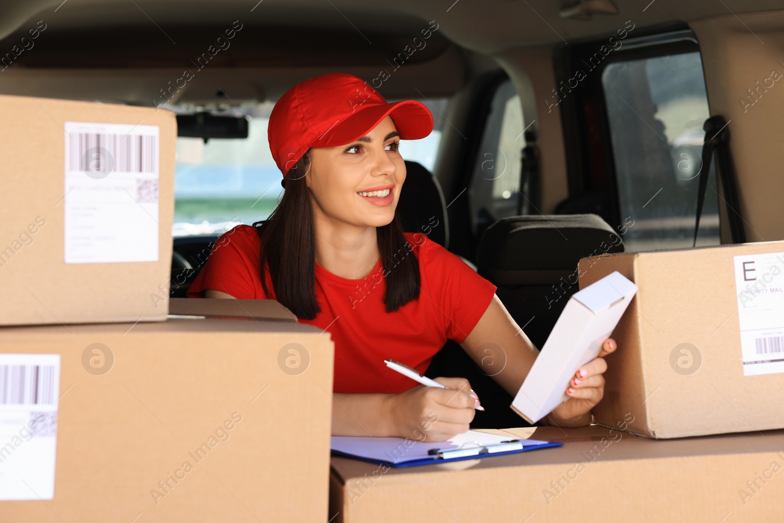 Photo of Courier with clipboard checking packages in delivery van