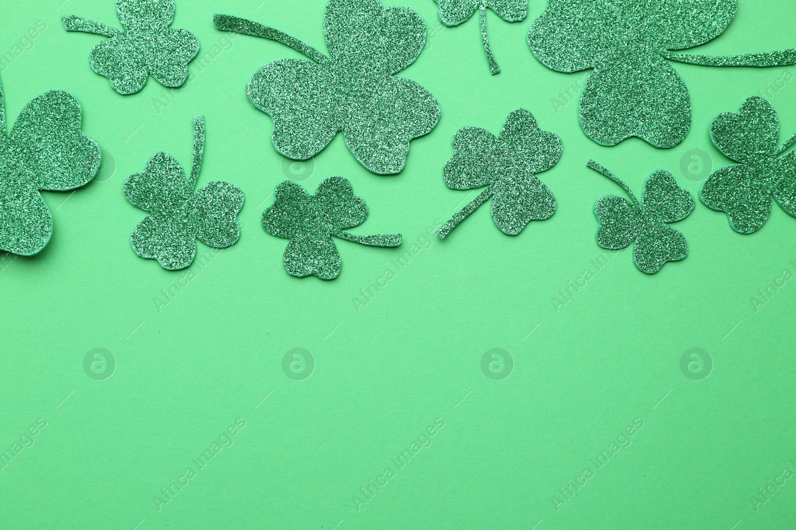 Photo of St. Patrick's day. Shiny decorative clover leaves on green background, flat lay. Space for text