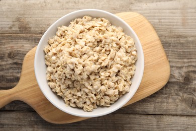 Photo of Tasty boiled oatmeal in bowl on wooden table, top view