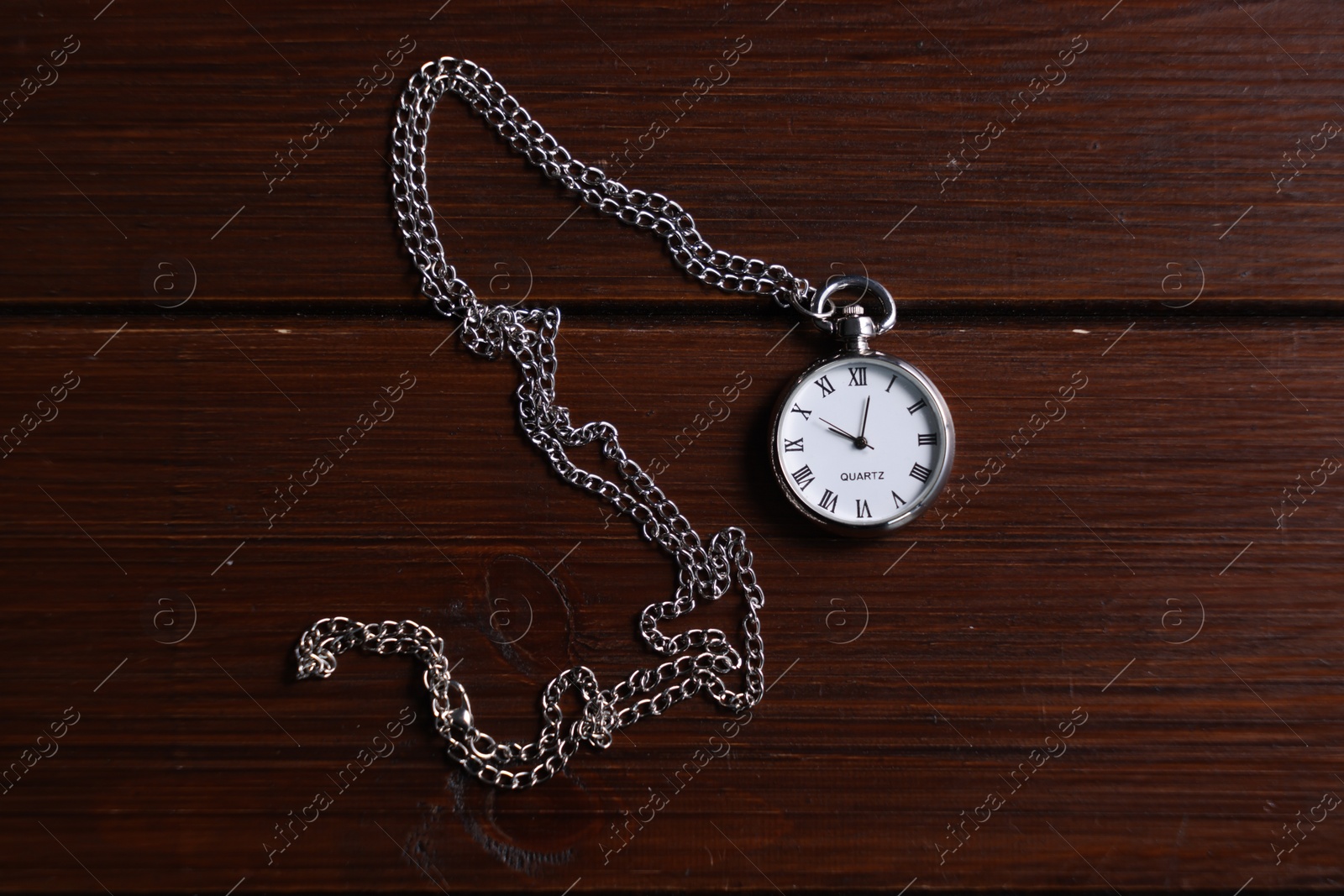 Photo of Silver pocket clock with chain on wooden table, top view
