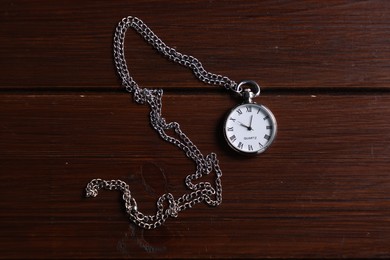 Silver pocket clock with chain on wooden table, top view
