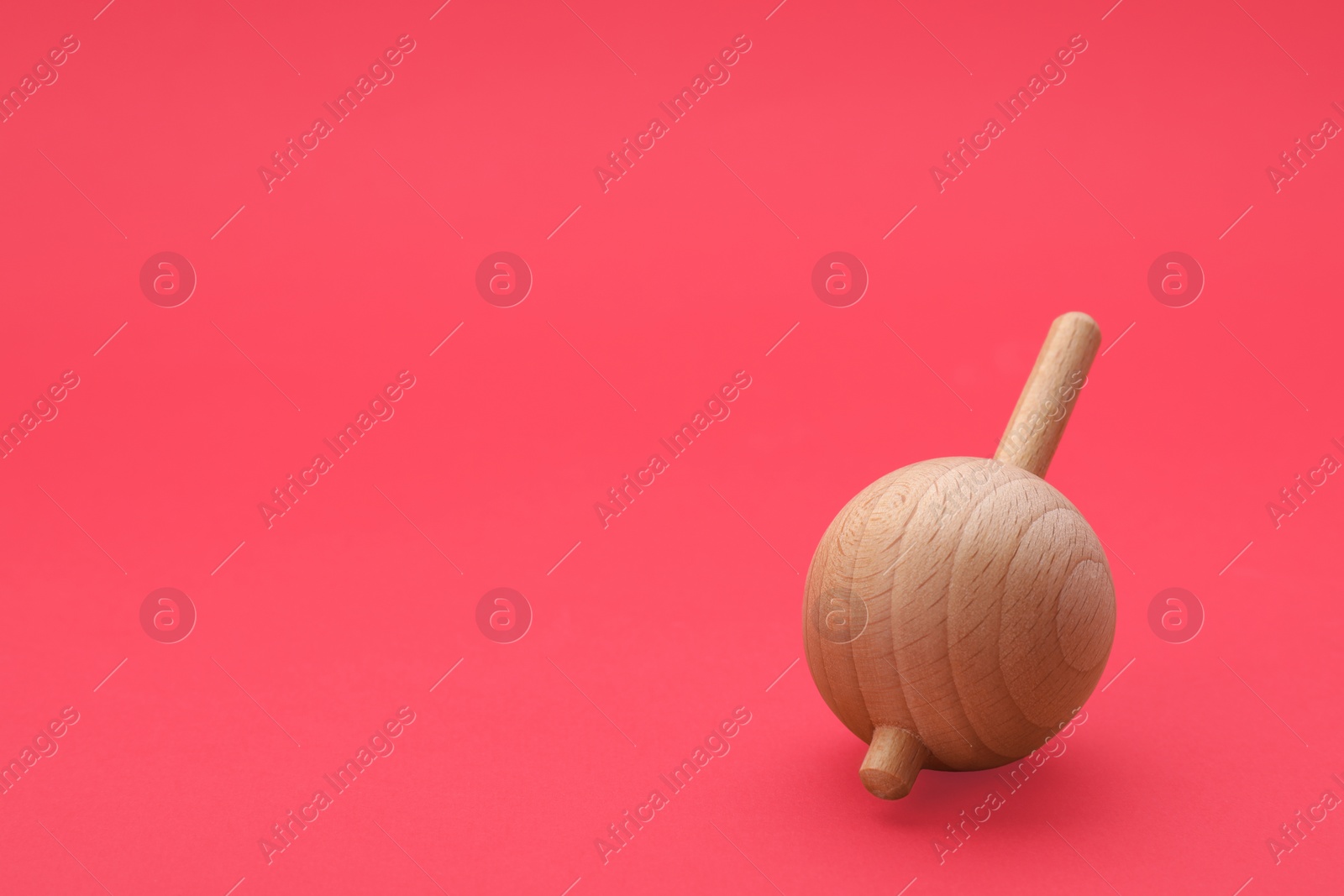 Photo of One wooden spinning top on red background, space for text. Toy whirligig