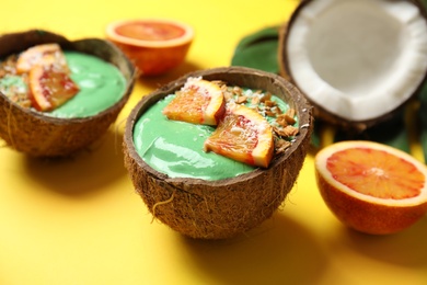 Coconut shells with yummy spirulina smoothie and oranges on color background, closeup